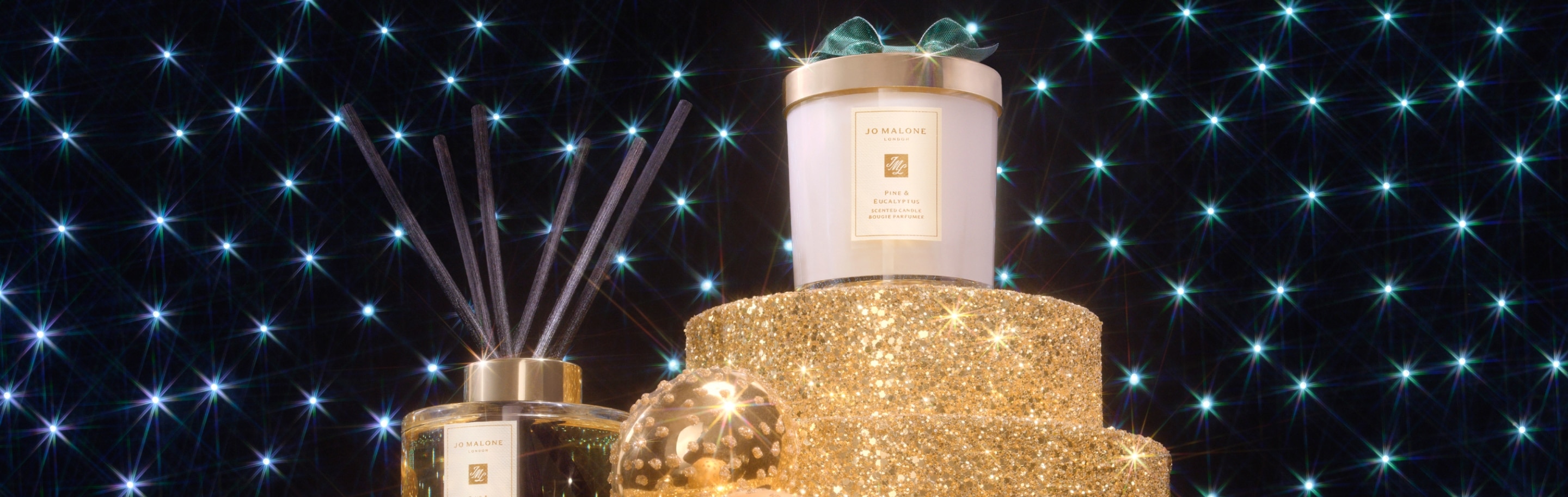 Jo Malone London Pine and Eucalyptus Home Candle and Diffuser on glittering gold plinths with spotlight background